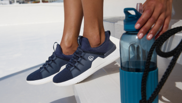 Close-up of feet in dark blue trainers next to a turquoise water bottle on a light background. A hand reaches for the bottle.