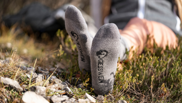 Close-up of soles of feet in grey Giesswein socks with black logo on a lawn.