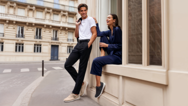 A young couple is standing and sitting in front of a classic Parisian townhouse. 