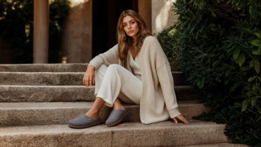 Woman in beige loungewear outfit sitting relaxed on stone steps wearing dark grey Giesswein wool shoes