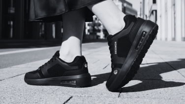 Black and white close-up of a black Giesswein sneaker with air chamber sole on the feet of a person on city pavement.