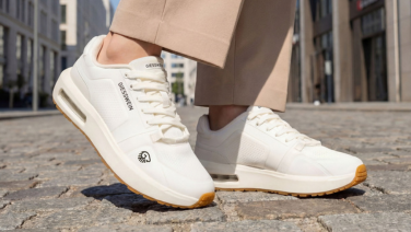 Close-up of white Giesswein trainers with air chamber soles and honey-coloured outsoles on cobblestones.