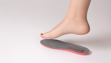 A bare foot with red nail polish hovers above a grey Giesswein insole with a red edge on a white background.